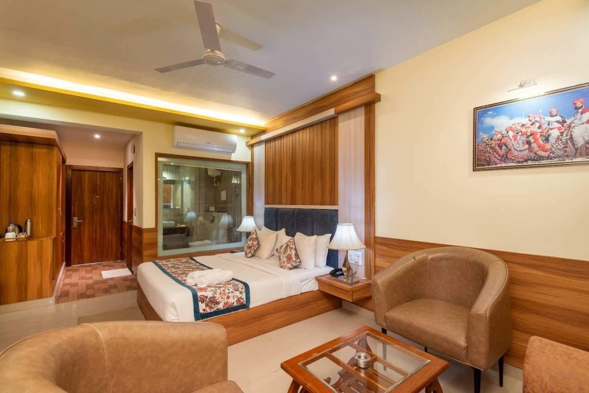Habitación de hotel con una cama, dos sillones, una mesita de centro, un ventilador de techo y un cuadro en la pared.