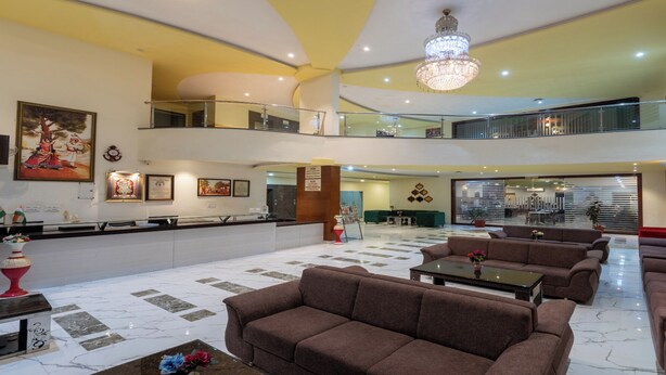 A spacious lobby with multiple seating areas, a reception desk, and a chandelier. - Hotel Kaushal International (Sanchor)