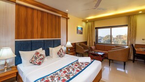 A hotel room with a large bed, a desk, a chair, and a view of the outdoors. - Hotel Kaushal International (Sanchor)