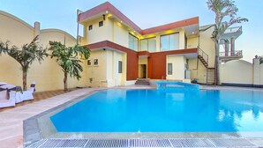 A modern hotel with a swimming pool, a covered outdoor seating area, and a staircase leading to a balcony. - Hotel Kaushal International (Sanchor)