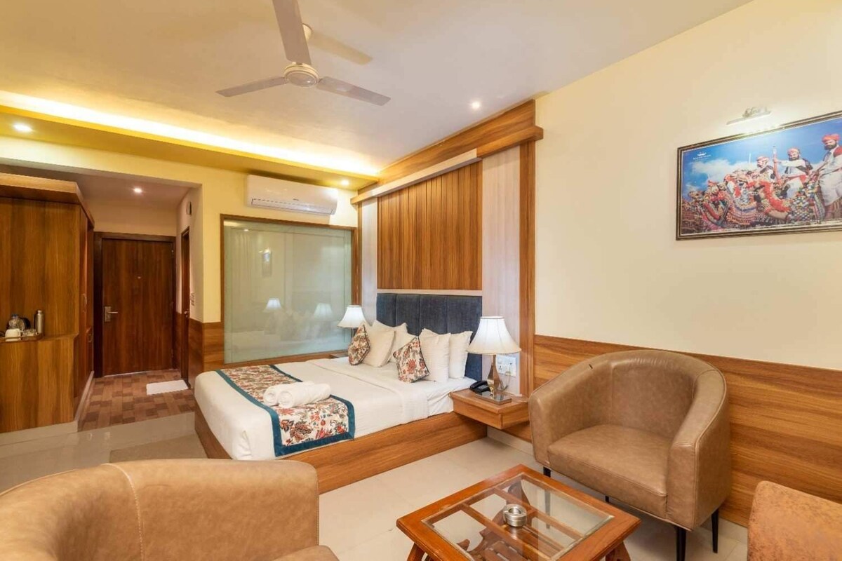 Une chambre d’hôtel avec un lit, deux chaises, une table basse, un ventilateur de plafond et un tableau au mur.