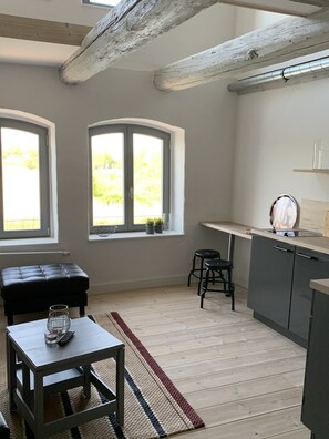 A modern kitchen with a wooden ceiling, a dining area with a table and chairs, and large windows with a view of greenery.