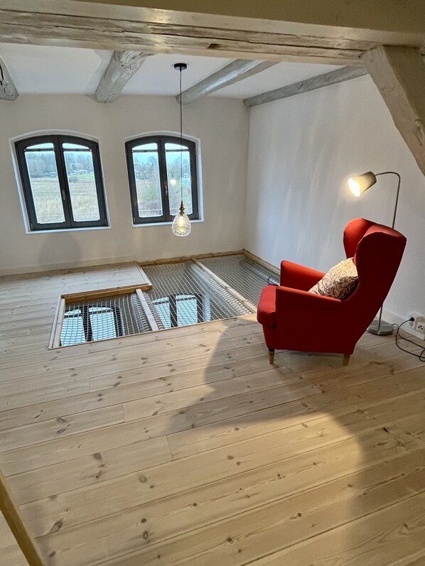 A high-ceiling room with a sloped ceiling, two windows, a red chair, a hanging light fixture, and a wooden floor.