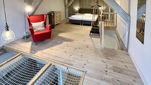 Ein Schlafzimmer im Loft-Stil mit freiliegenden Holzbalken, einem roten Sessel, einem Bett und einer Leiter.