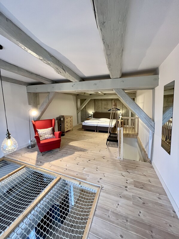 A loft bedroom with exposed wooden beams, a red armchair, a bed, and a ladder.