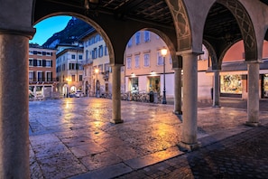 An open courtyard with stone flooring, arches, and buildings in the background.