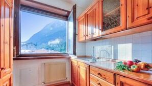 A kitchen with wooden cabinets, a window with a view of mountains, a radiator, and a countertop with vegetables. - Casa Palmaverde Few Min From Lake (Riva del Garda)