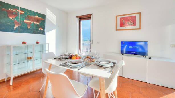 A dining area with a table set for two, a television on a stand, and a world map on the wall. - Casa Palmaverde Few Min From Lake (Riva del Garda)