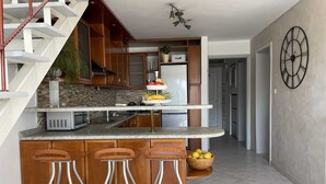 Une cuisine moderne avec un îlot central, des tabourets de bar en bois, un escalier et une horloge au mur.