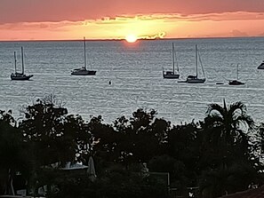 A sunset over the ocean with several sailboats. - Studio with ocean view, beach, air conditioning, pool, bar-restaurant, car rental (Sainte-Anne)