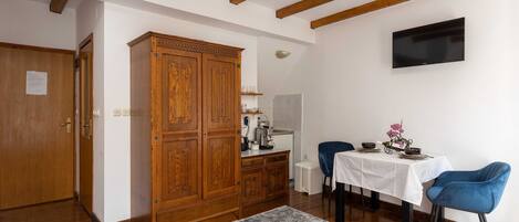 A room with wooden beams, a TV mounted on the wall, a dining table with chairs, and a cabinet.