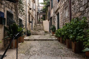 Un estrecho callejón empedrado con escalones que conducen a la entrada de un edificio, flanqueado por macetas y paredes de piedra.