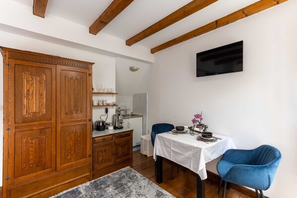 Un comedor con un aparador de madera, una mesa blanca con una silla azul y un televisor montado en la pared.