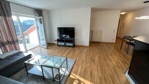 Uma sala de estar moderna com televisão de tela plana, mesa de centro de vidro, sofá e área de jantar com mesa e cadeiras.