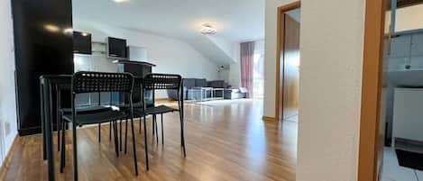 A modern kitchen with a built-in oven and microwave, a dining area with a wooden table and chairs, and a large window providing natural light.