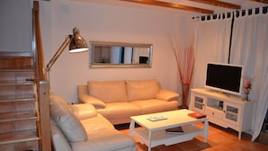En stue med sofa, sofabord, fjernsyn på et stativ, lampe og trappe.