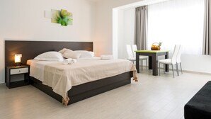 A modern hotel room with a large bed, bedside table, and a dining area with chairs and a table. - Villa Kabalero (Konavle)