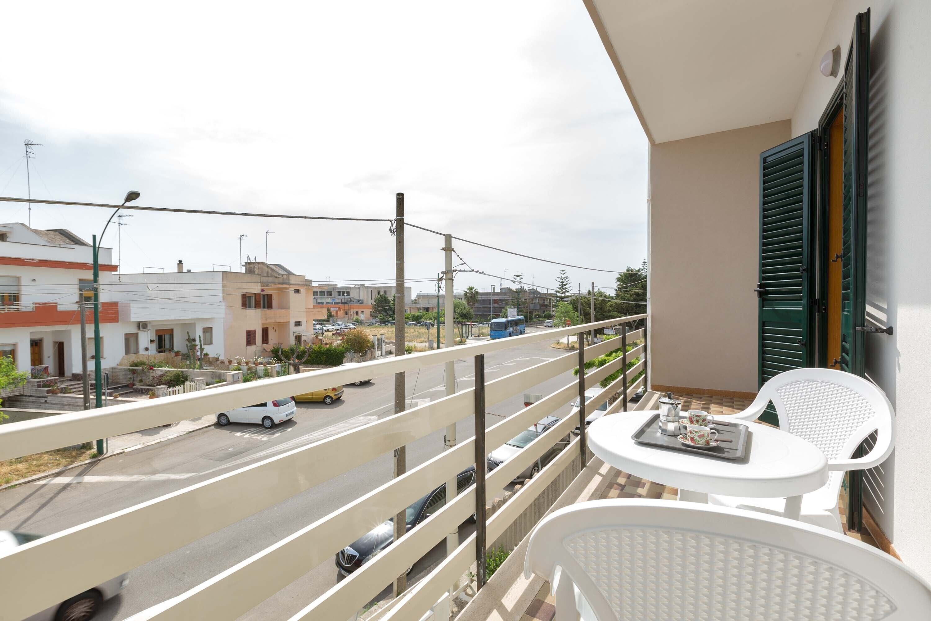 Ein Balkon mit weißem Tisch und Stühlen, mit Blick auf eine Straße mit Autos und Gebäuden.