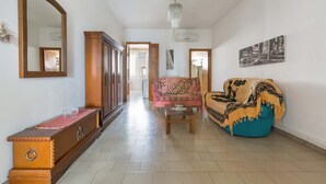 Un salon spacieux avec un meuble en bois, un canapé, un fauteuil et un lustre suspendu.