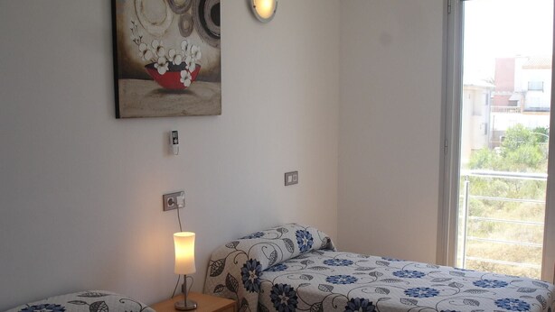 A bedroom with two beds, a bedside table with a lamp, a wall-mounted light, and a painting above the beds. - PICAFORT1, PRIVATE POOL, free wifi, beach, air conditioning, barbecue (Ca'n picafort)
