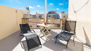 A balcony with a table and chairs, a view of the cityscape, and a clear sky.