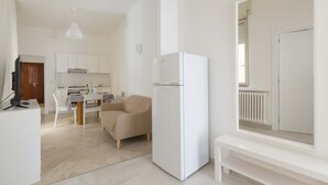 A modern, minimalistic living space with a kitchenette, a sofa, a dining table, and a white refrigerator. - 2483 La Casa di Maristella - Trilo by Barbarhouse (Otranto)