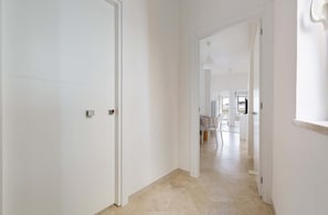Corredor com paredes e portas brancas, que leva a uma sala de jantar com mesa e cadeiras.
