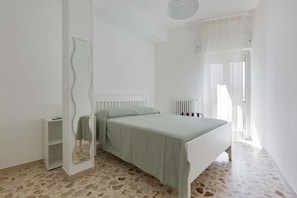 Quarto com cama, espelho, radiador e janela com cortinas.