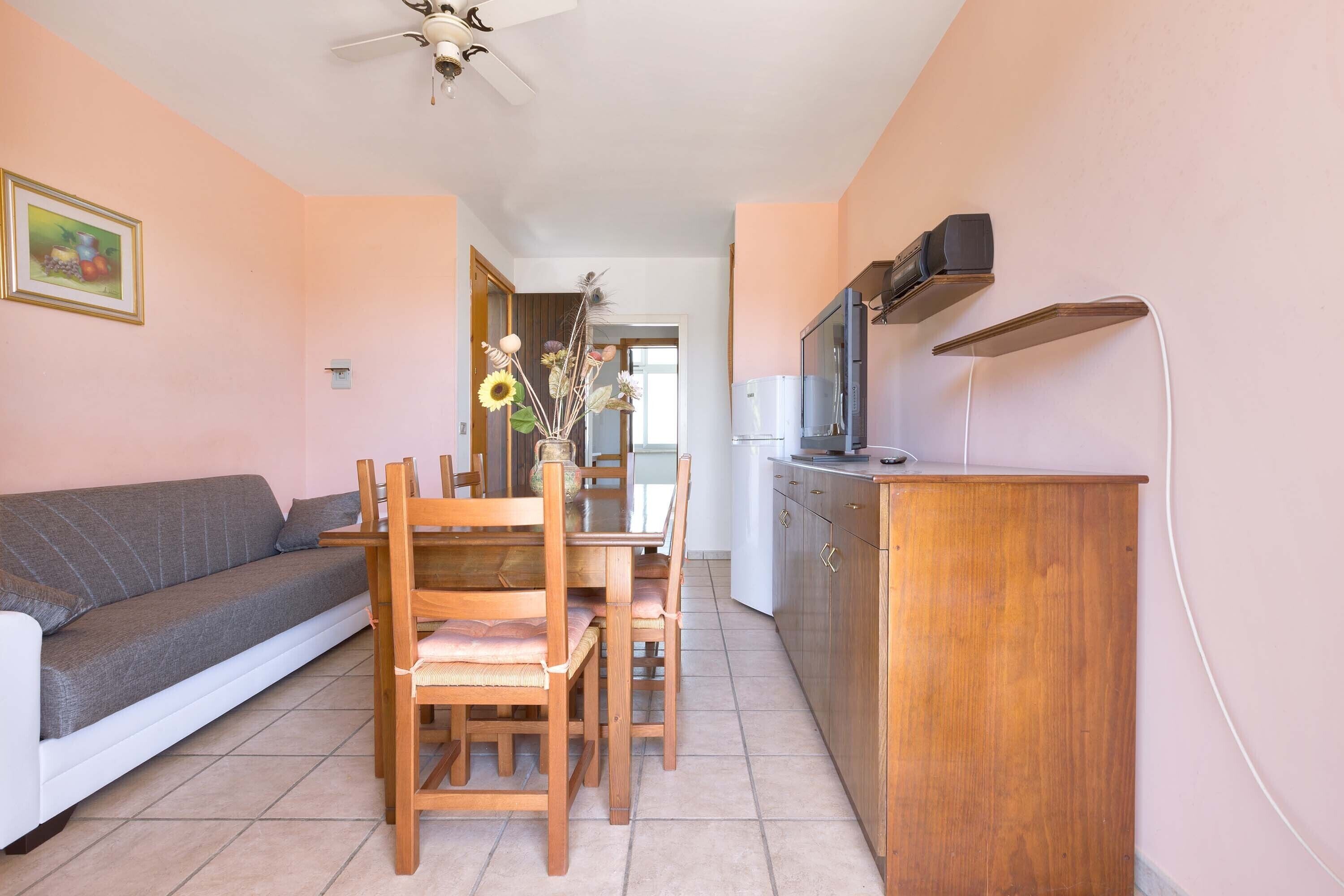 Una sala de estar con sofá, mesa de comedor, sillas, televisor y aparador de madera.
