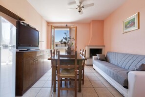 A dining area with a wooden table and chairs, a television on the left, and a sofa on the right.