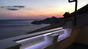 A balcony with a view of the sea at sunset, a stone wall, and a railing. - Apartment H&D (Dubrovnik)
