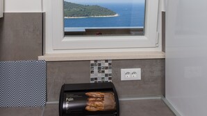 A kitchen with a window overlooking a coastal view, a toaster, and a tiled backsplash. - Apartment H&D (Dubrovnik)