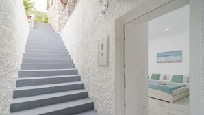 A staircase leading to a bedroom with a bed, a painting, and a white door. - Apartment Rafaello (Dubrovnik)