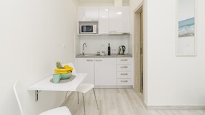 A compact kitchen with white cabinets, a microwave, and a small dining area with a table and chairs. - Apartment Rafaello (Dubrovnik)