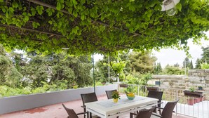 A covered patio with a table and chairs, surrounded by potted plants and a view of greenery. - Apartment Rafaello (Dubrovnik)