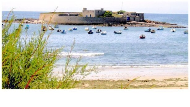 A coastal scene with boats, a fortified structure, and a beach.
