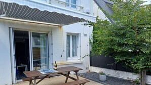 A patio with a wooden table and chairs, a bottle of champagne, and a small table with a glass.