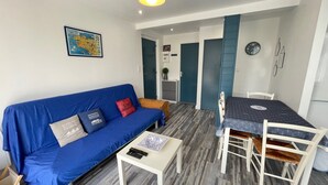 A modern living room with a blue sofa, a small white table, and a dining area with a table and chairs.