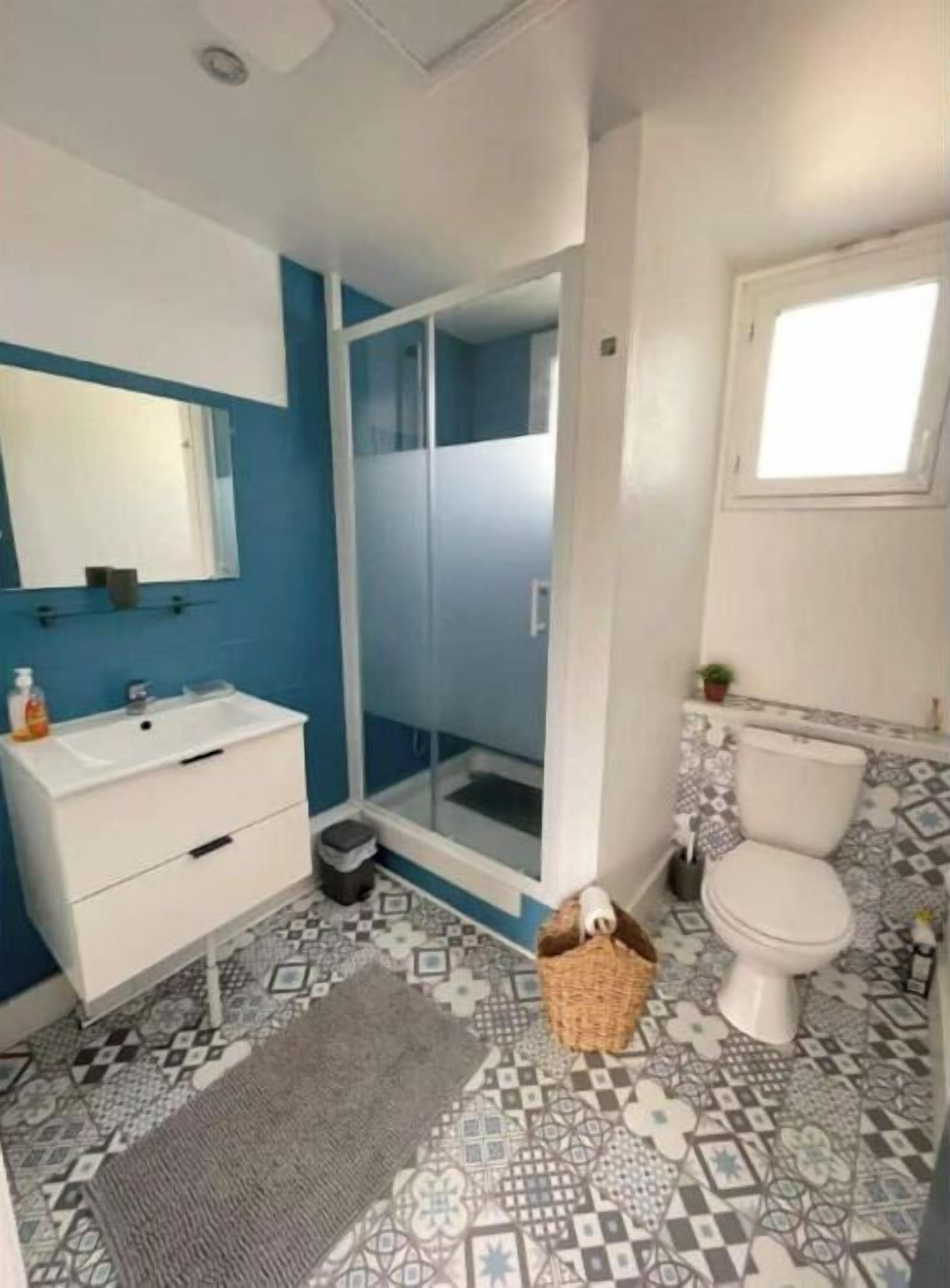 A bathroom with a white sink, a mirror, a shower enclosure, a toilet, and patterned floor tiles.