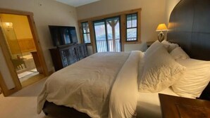 A bedroom with a large bed, a TV, and a window with a view of trees. - Ski In / Ski Out Treetops Home with Outdoor Private Spa (Stratton)