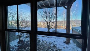 A view through a window with a wooden frame, showing a snowy outdoor area with a wooden structure and bare trees. - Ski In / Ski Out Treetops Home with Outdoor Private Spa (Stratton)