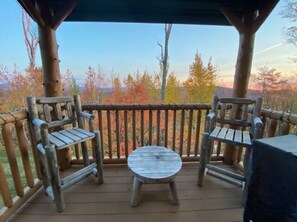 Relax on the deck with a clear view of the surrounding landscape, featuring a comfortable seating area with two chairs and a small table.