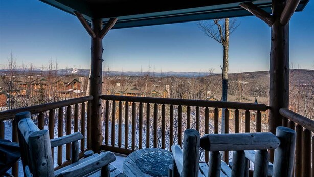 A wooden deck with a view of a snowy landscape and buildings in the distance. - Ski In / Ski Out Treetops Home with Outdoor Private Spa (Stratton)