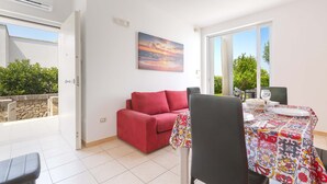 A bright room with a red sofa, a dining table with a colorful tablecloth, and a painting of a sunset on the wall. - 3046 Villetta Bianca by Barbarhouse (Otranto)
