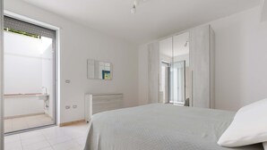 A bedroom with a bed, a wardrobe, a bathroom with a shower, and a large window. - 3046 Villetta Bianca by Barbarhouse (Otranto)
