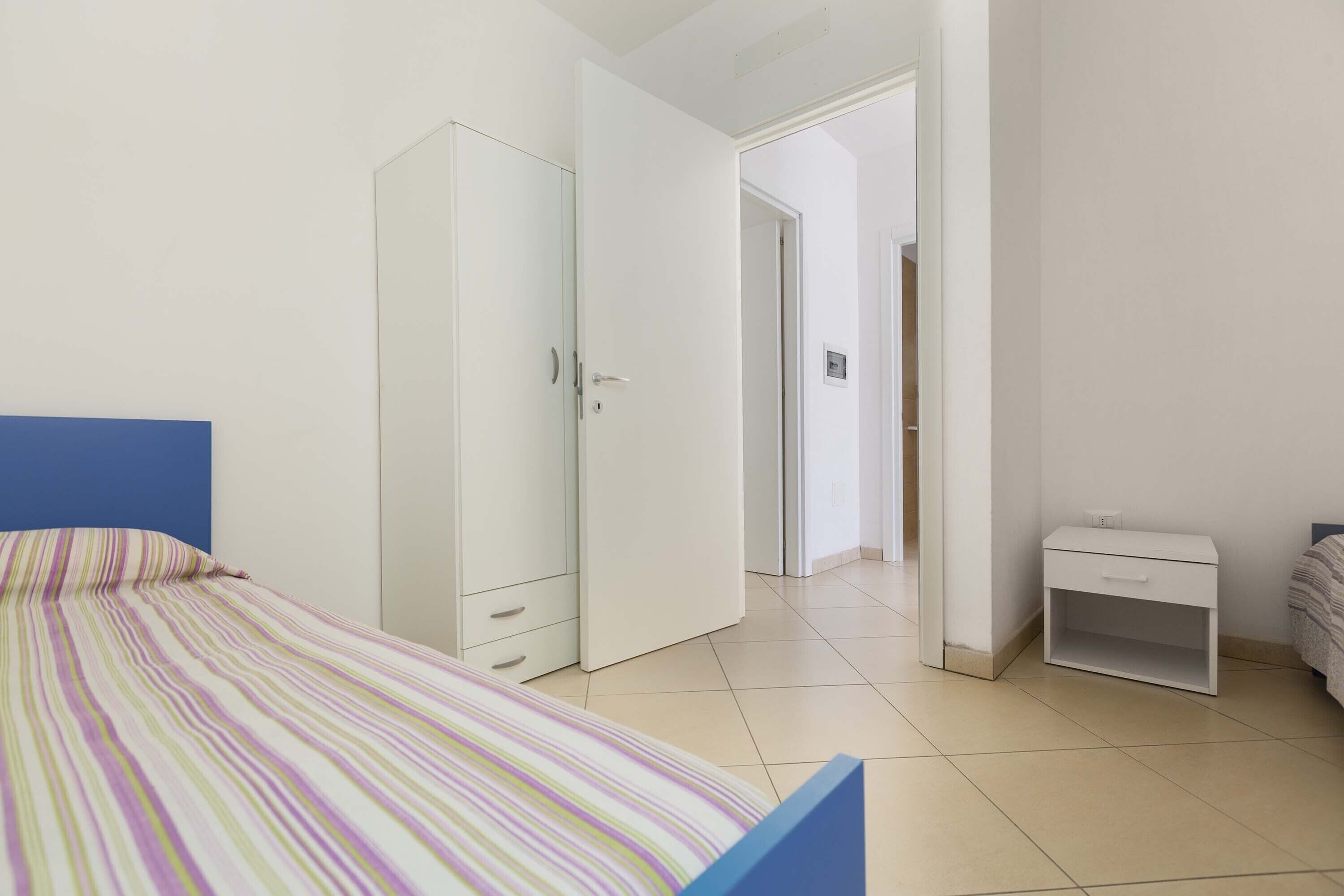 A bedroom with a bed, a wardrobe, a nightstand, and a door leading to another room.
