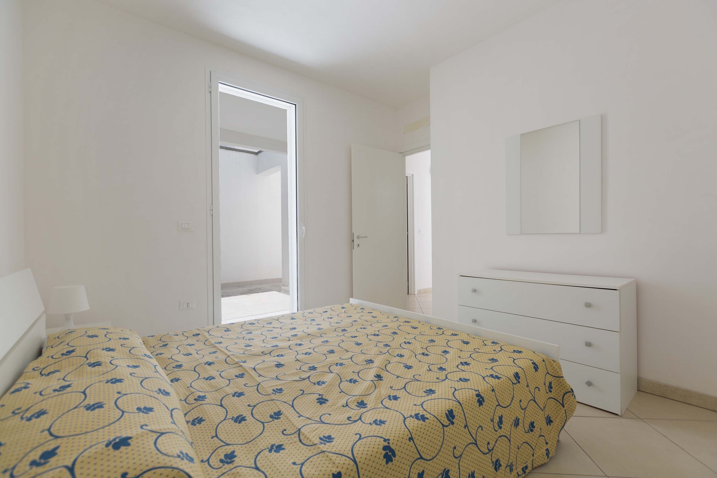 Une chambre à coucher comprenant un lit, une commode, un miroir et une porte donnant sur une autre pièce.
