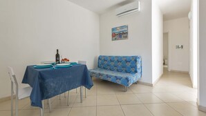 A dining area with a table set for two, a blue sofa, and a wall-mounted air conditioner. - 2371 Villette Girovagando - Trilo Superior by Barbarhouse (Melendugno)
