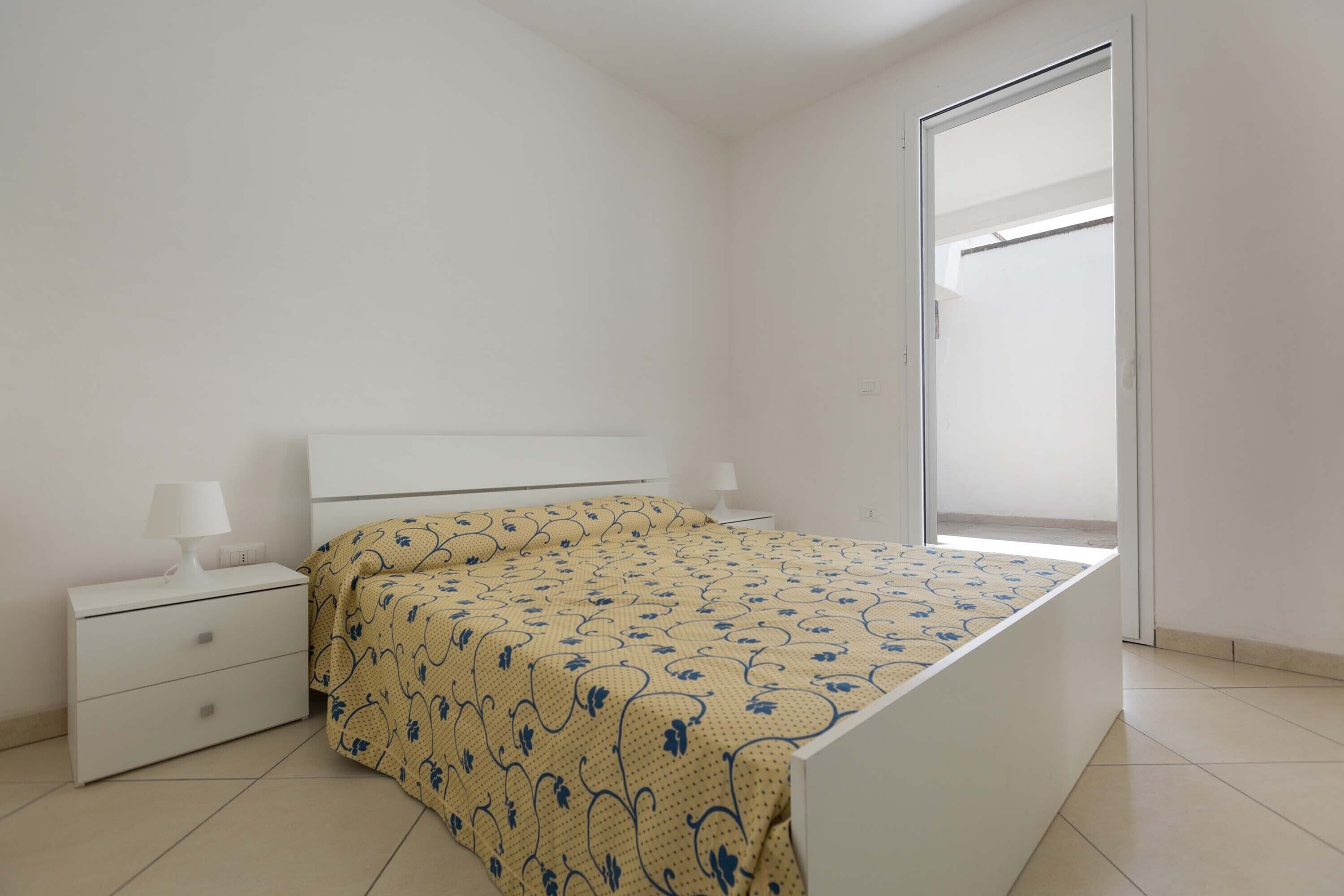 Een slaapkamer met een bed, nachtkastje, lamp en raam.
