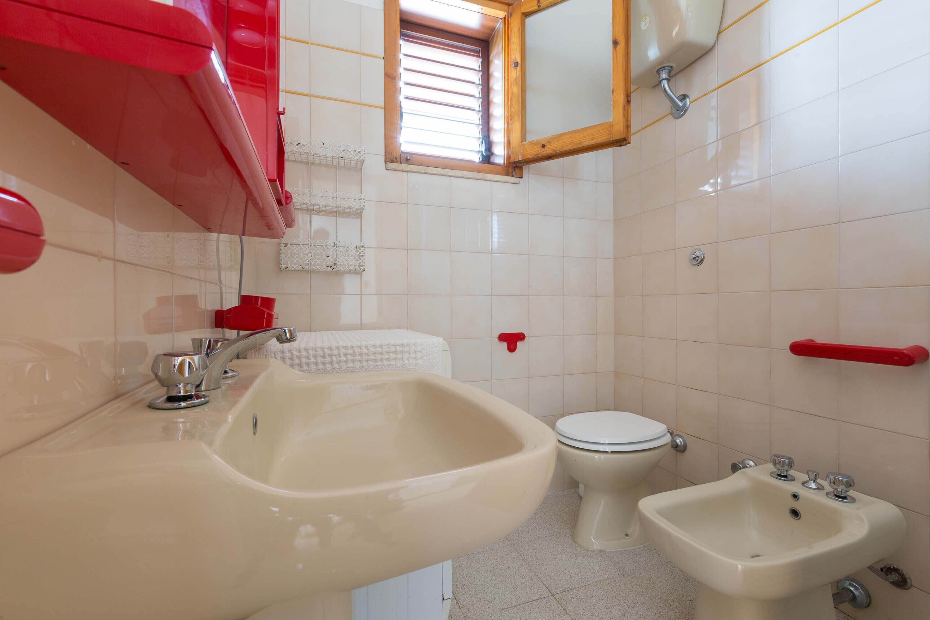 A bathroom with a sink, bidet, toilet, and a window with blinds.